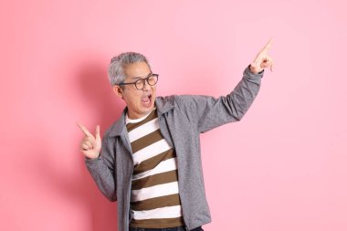 40 'lı yaşlarda Asyalı bir adam pembe arka planda sıradan kıyafetlerle dolanıyor..