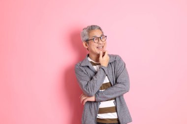 40 'lı yaşlarda Asyalı bir adam pembe arka planda sıradan kıyafetlerle dolanıyor..