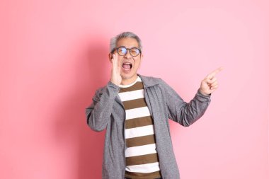 40 'lı yaşlarda Asyalı bir adam pembe arka planda sıradan kıyafetlerle dolanıyor..