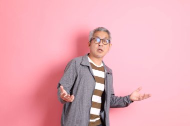 40 'lı yaşlarda Asyalı bir adam pembe arka planda sıradan kıyafetlerle dolanıyor..