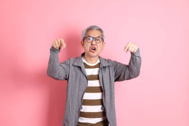 40 'lı yaşlarda Asyalı bir adam pembe arka planda sıradan kıyafetlerle dolanıyor..