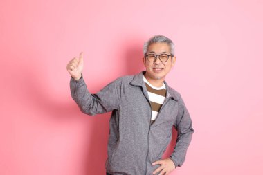 40 'lı yaşlarda Asyalı bir adam pembe arka planda sıradan kıyafetlerle dolanıyor..