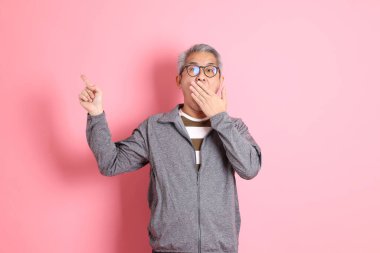 40 'lı yaşlarda Asyalı bir adam pembe arka planda sıradan kıyafetlerle dolanıyor..