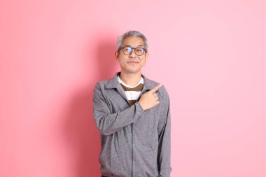 40 'lı yaşlarda Asyalı bir adam pembe arka planda sıradan kıyafetlerle dolanıyor..