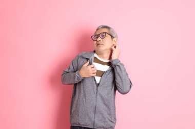 40 'lı yaşlarda Asyalı bir adam pembe arka planda sıradan kıyafetlerle dolanıyor..