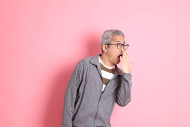 40 'lı yaşlarda Asyalı bir adam pembe arka planda sıradan kıyafetlerle dolanıyor..