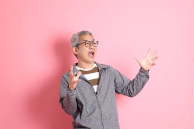 40 'lı yaşlarda Asyalı bir adam pembe arka planda sıradan kıyafetlerle dolanıyor..