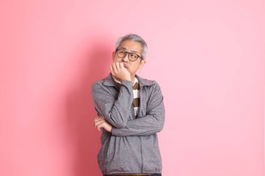 40 'lı yaşlarda Asyalı bir adam pembe arka planda sıradan kıyafetlerle dolanıyor..