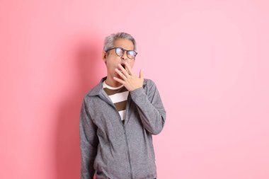 40 'lı yaşlarda Asyalı bir adam pembe arka planda sıradan kıyafetlerle dolanıyor..