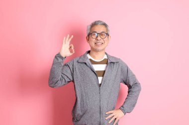 40 'lı yaşlarda Asyalı bir adam pembe arka planda sıradan kıyafetlerle dolanıyor..