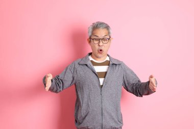 40 'lı yaşlarda Asyalı bir adam pembe arka planda sıradan kıyafetlerle dolanıyor..