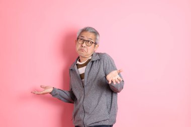 40 'lı yaşlarda Asyalı bir adam pembe arka planda sıradan kıyafetlerle dolanıyor..