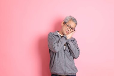 40 'lı yaşlarda Asyalı bir adam pembe arka planda sıradan kıyafetlerle dolanıyor..