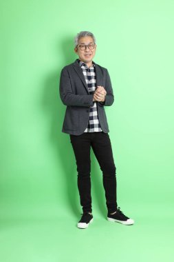 40 'lı yaşlarda Asyalı bir adam yeşil arka planda şık günlük kıyafetlerle takılıyor..