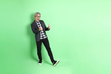 40 'lı yaşlarda Asyalı bir adam yeşil arka planda şık günlük kıyafetlerle takılıyor..