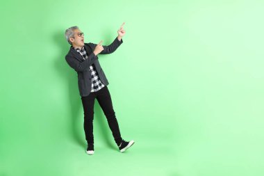 40 'lı yaşlarda Asyalı bir adam yeşil arka planda şık günlük kıyafetlerle takılıyor..