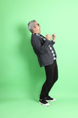 40 'lı yaşlarda Asyalı bir adam yeşil arka planda şık günlük kıyafetlerle takılıyor..