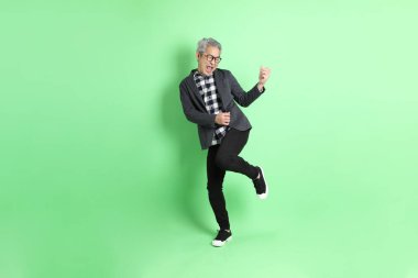 40 'lı yaşlarda Asyalı bir adam yeşil arka planda şık günlük kıyafetlerle takılıyor..