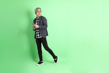 40 'lı yaşlarda Asyalı bir adam yeşil arka planda şık günlük kıyafetlerle takılıyor..