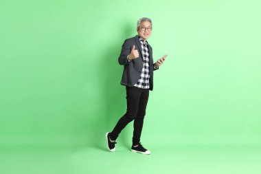 40 'lı yaşlarda Asyalı bir adam yeşil arka planda şık günlük kıyafetlerle takılıyor..