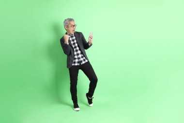 40 'lı yaşlarda Asyalı bir adam yeşil arka planda şık günlük kıyafetlerle takılıyor..