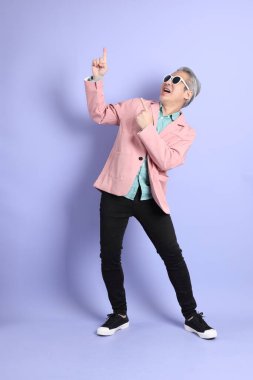 40 'lı yaşlarda Asyalı bir adam mor arka planda şık günlük kıyafetlerle dikiliyor..