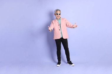 40 'lı yaşlarda Asyalı bir adam mor arka planda şık günlük kıyafetlerle dikiliyor..