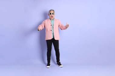 40 'lı yaşlarda Asyalı bir adam mor arka planda şık günlük kıyafetlerle dikiliyor..