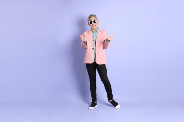 40 'lı yaşlarda Asyalı bir adam mor arka planda şık günlük kıyafetlerle dikiliyor..