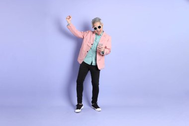 40 'lı yaşlarda Asyalı bir adam mor arka planda şık günlük kıyafetlerle dikiliyor..