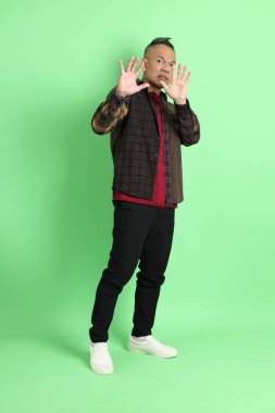 Yeşil arka planda duran ekose gömlekli 40 'lı yaşlardaki Asyalı adam..