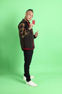 Yeşil arka planda duran ekose gömlekli 40 'lı yaşlardaki Asyalı adam..