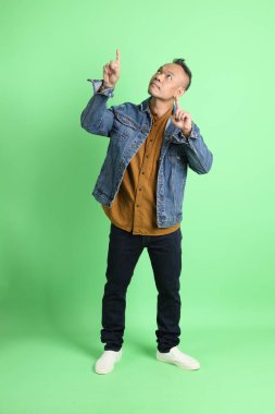 Yeşil arka planda duran kot gömlekli 40 'lı yaşlardaki Asyalı adam..