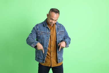 Yeşil arka planda duran kot gömlekli 40 'lı yaşlardaki Asyalı adam..