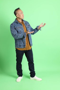 Yeşil arka planda duran kot gömlekli 40 'lı yaşlardaki Asyalı adam..