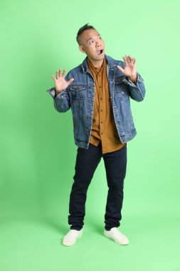 Yeşil arka planda duran kot gömlekli 40 'lı yaşlardaki Asyalı adam..