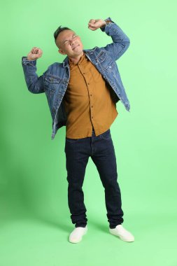 Yeşil arka planda duran kot gömlekli 40 'lı yaşlardaki Asyalı adam..