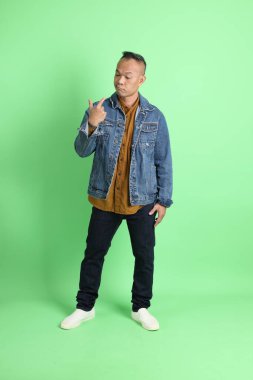 Yeşil arka planda duran kot gömlekli 40 'lı yaşlardaki Asyalı adam..