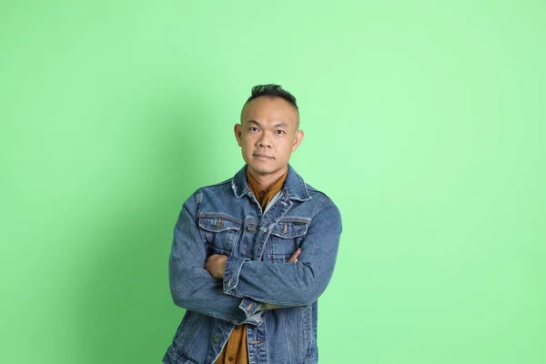 Yeşil Arka Planda Duran Kot Gömlekli Yaşlardaki Asyalı Adam — Stok fotoğraf