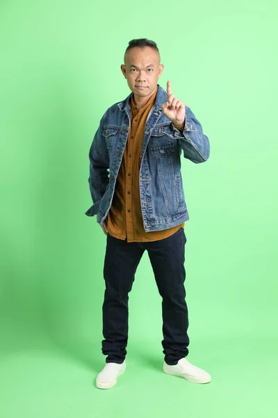 40多岁的亚洲男子穿着牛仔衬衫站在绿色的背景上 — 图库照片