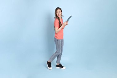 The young adult Asian woman with casual clothes with jeans standing on the blue background.