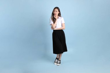 The young Asian student with uniform standing on the blue background.