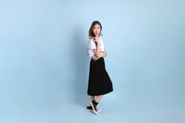 The young Asian student with uniform standing on the blue background.