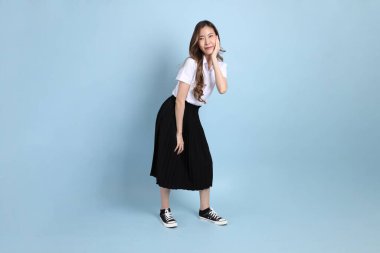 The young Asian student with uniform standing on the blue background.