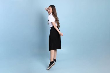 The young Asian student with uniform standing on the blue background.