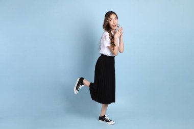 The young Asian student with uniform standing on the blue background.