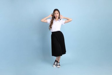 The young Asian student with uniform standing on the blue background.