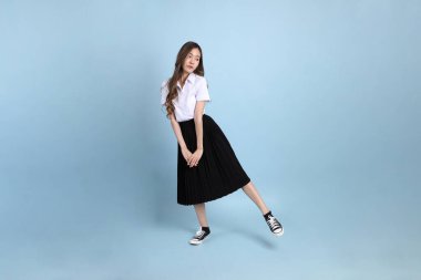 The young Asian student with uniform standing on the blue background.
