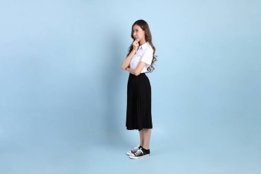 The young Asian student with uniform standing on the blue background.