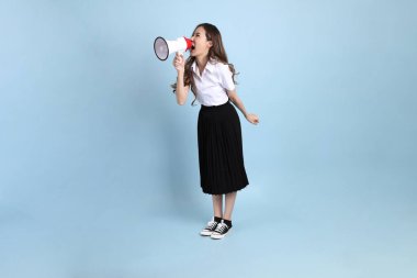 The young Asian student with uniform standing on the blue background.
